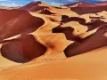 Pomarańczowe wydmy Namibii o zachodzie słońca, z widocznymi cieniami i falami piasku.
