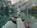Drewniane łodzie przy drewnianym pomoście na spokojnym Lago di Braies, odbijające się w tafli wody, z majestatycznymi górami w tle.