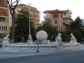 Fontanna z rzeźbami dzieci i kulą w centrum, otoczona budynkami w Marina di Massa.