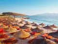 Albania, lipiec: słoneczna plaża z rzędami parasoli i leżaków, turkusowe morze i góry w tle. Idealna pogoda na wakacje.