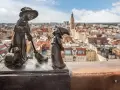 Figurki krasnali: czarownica z kotem i miotłą, na tle panoramy Wrocławia.