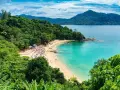Tropikalna plaża z turkusową wodą, zielonymi wzgórzami i leżakami.