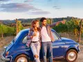 Para młoda przy niebieskim Fiat 500, podróżując samochodem do Włoch, podziwia toskańskie wzgórza.