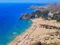 Widok z lotu ptaka na piaszczystą plażę z leżakami, turkusowe morze i górzysty krajobraz Rodos.