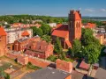 Zamek krzyżacki w Lęborku, z charakterystyczną wieżą i ceglaną architekturą, otoczony zielenią i zabudowaniami miejskimi.