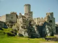 Ruiny zamku na skale, z wieżą i murami, na tle błękitnego nieba.