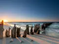 Zachód słońca nad Bałtykiem, zniszczone pale na plaży i spokojne fale.
