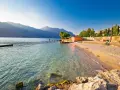 Słoneczna plaża nad jeziorem Garda z kamienistym brzegiem i łagodnymi falami.