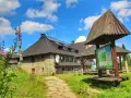 Kamienny schronisko na Turbaczu z dzieckiem w tle, otoczone zielenią i kwitnącymi kwiatami.