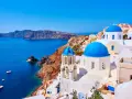 Santorini co zobaczyć: białe domy z niebieskimi kopułami kościołów na klifie, turkusowe morze i łodzie.