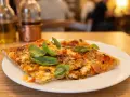Pyszna pizza na talerzu, idealna odpowiedź na pytanie: gdzie zjeść w Rzymie. W tle butelki z oliwą i widok na restaurację.