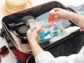 Pakowanie bagażu podręcznego: kosmetyki w małych buteleczkach, aparat, okulary i słomkowy kapelusz.