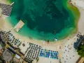 Widok z lotu ptaka na zatokę z turkusową wodą, plażą z leżakami i parasolami oraz łodziami.