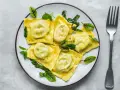 Pyszne ravioli z ricottą i szpinakiem, polane sosem, ozdobione świeżymi ziołami. Obok leży widelec.