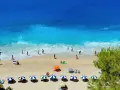 Plaża z turkusową wodą, piaskiem i ludźmi odpoczywającymi pod parasolami.