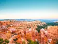 Zachód słońca nad Bryce National Park. Wąwóz pełen pomarańczowych hoodoos i zielonych drzew, z turystami na szlaku.