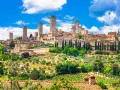 Widok na średniowieczne wieże i zabudowania San Gimignano w Toskanii, otoczone zielenią i winnicami.