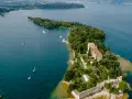Malowniczy widok na Isola del Garda z pałacem i ogrodami, otoczony turkusową wodą jeziora.