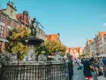 Fontanna Neptuna na tle kamienic i tłumu ludzi w Gdańsku.