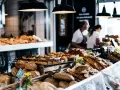 Stoisko z pieczywem i ciastami, przypominające najtańsze supermarkety we Włoszech. W tle widać sprzedawców.