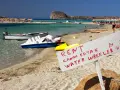 Maj na Krecie: plaża z leżakami, turkusowa woda, łódki i tablica z ofertą wynajmu kajaków i rowerów wodnych.