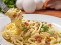 Pyszne spaghetti carbonara przepis na talerzu, z widocznymi jajkami i boczkiem w tle. Idealne danie dla miłośników włoskiej kuchni.