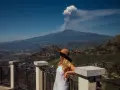 Kobieta w kapeluszu patrzy na dymiący wulkan Etna z tarasu widokowego.
