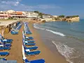 Rzędy leżaków i parasoli na piaszczystej plaży, z hotelami w tle. Idealne miejsce, by odpocząć i zastanowić się, gdzie na Korfu wybrać się na wakacje.