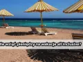 Plaża z leżakami i parasolami pod żółto-białymi pasami, turkusowe morze i błękitne niebo.