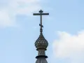 Drewniany krzyż prawosławny na tle błękitnego nieba z chmurami.