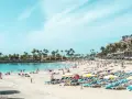 Tłum ludzi na plaży z leżakami i palmami. Idealne miejsce, by sprawdzić, która wyspa kanaryjska najcieplejsza w grudniu.