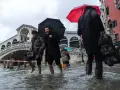 Ludzie brodzą w wodzie podczas acqua alta w Wenecji. Most Rialto w tle, deszcz i parasole.