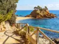 Ścieżka z drewnianą balustradą prowadzi do urokliwej zatoczki z piaszczystą plażą i skalistą wysepką. To idealne miejsce na odkrywanie uroków Costa Brava.