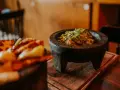 Świeże guacamole w kamiennym moździerzu, obok talerza z innymi najpopularniejszymi daniami meksykańskimi.