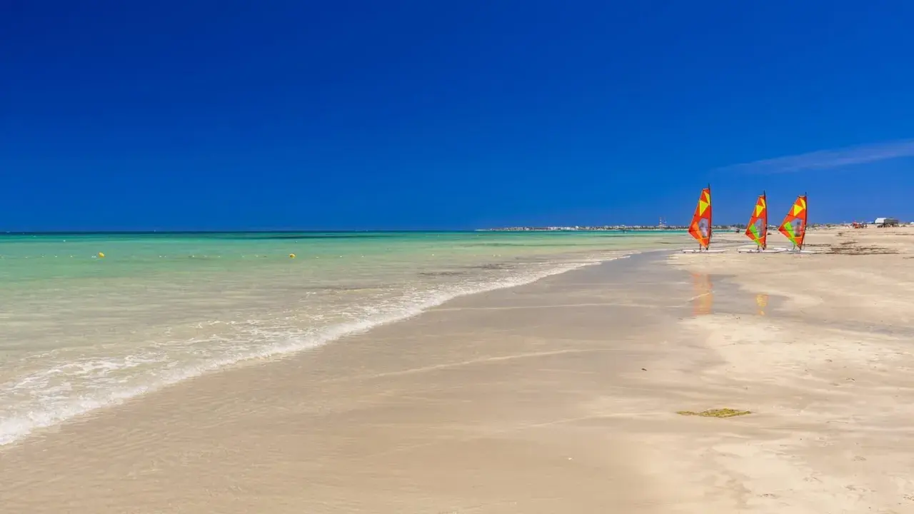 Piękna, słoneczna plaża w Tunezji. Idealna pogoda w maju na windsurfing, o czym świadczą trzy kolorowe żagle na piasku.