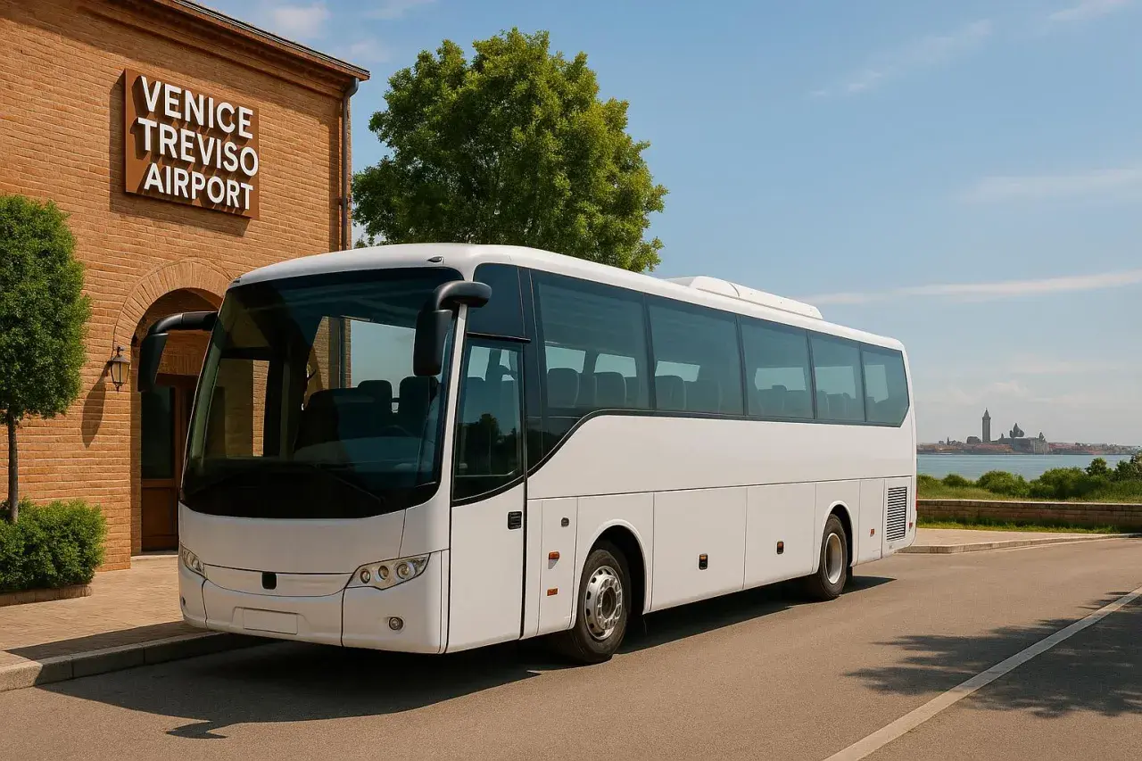 Biały autokar czeka na pasażerów przy budynku z napisem VENICE TREVISO AIRPORT. W tle widać panoramę Wenecji.