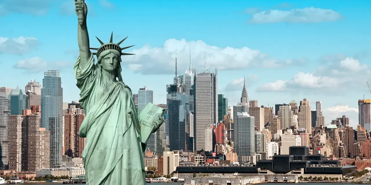 Statua Wolności wita podczas podróży do USA. W tle panorama Nowego Jorku z drapaczami chmur i statkami na rzece.