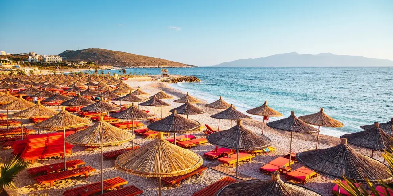 Albania, lipiec: słoneczna plaża z rzędami parasoli i leżaków, turkusowe morze i góry w tle. Idealna pogoda na wakacje.