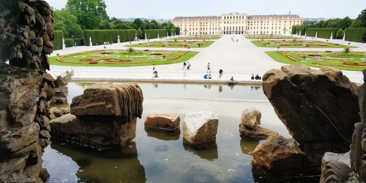 Wiedeń ogrody Sisi: malowniczy widok na pałac Schönbrunn i jego kwieciste tarasy, z kamienną fontanną w pierwszym planie.