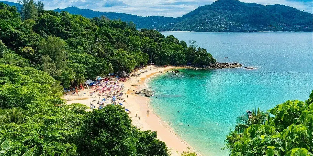 Tropikalna plaża z turkusową wodą, zielonymi wzgórzami i leżakami.