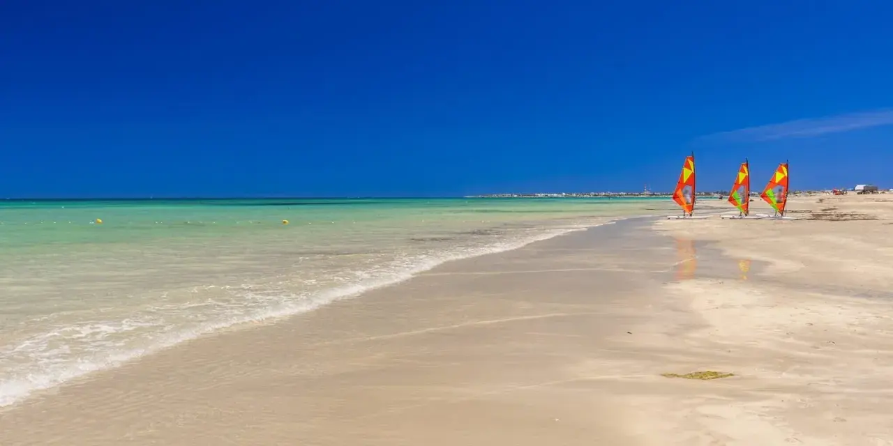 Piękna, słoneczna plaża w Tunezji. Idealna pogoda w maju na windsurfing, o czym świadczą trzy kolorowe żagle na piasku.