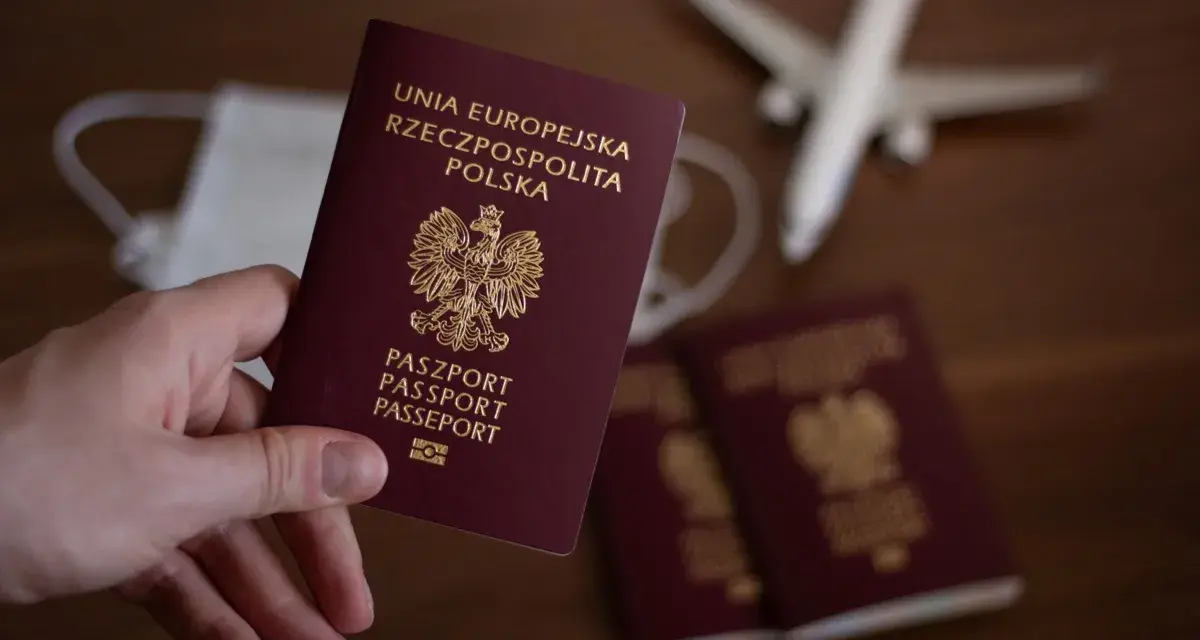 Dłoń trzyma polski paszport. Obok leżą kolejne dokumenty, maseczka i model samolotu. Zastanawiasz się, ile trwa wyrobienie paszportu?