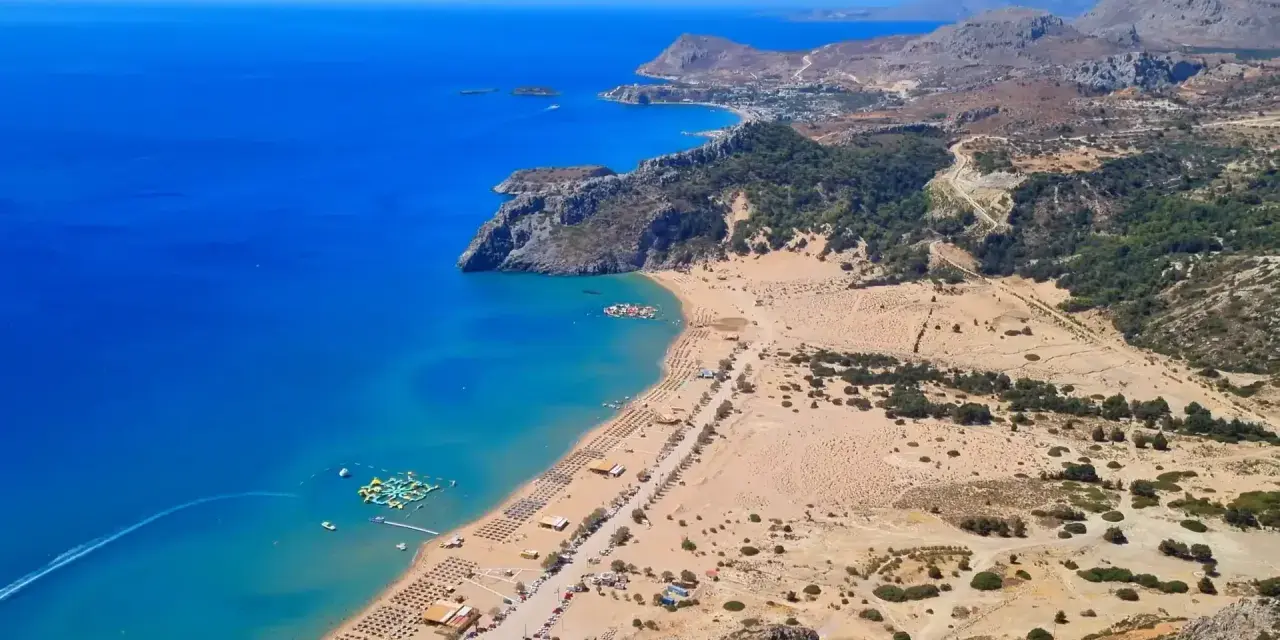 Widok z lotu ptaka na piaszczystą plażę z leżakami, turkusowe morze i górzysty krajobraz Rodos.