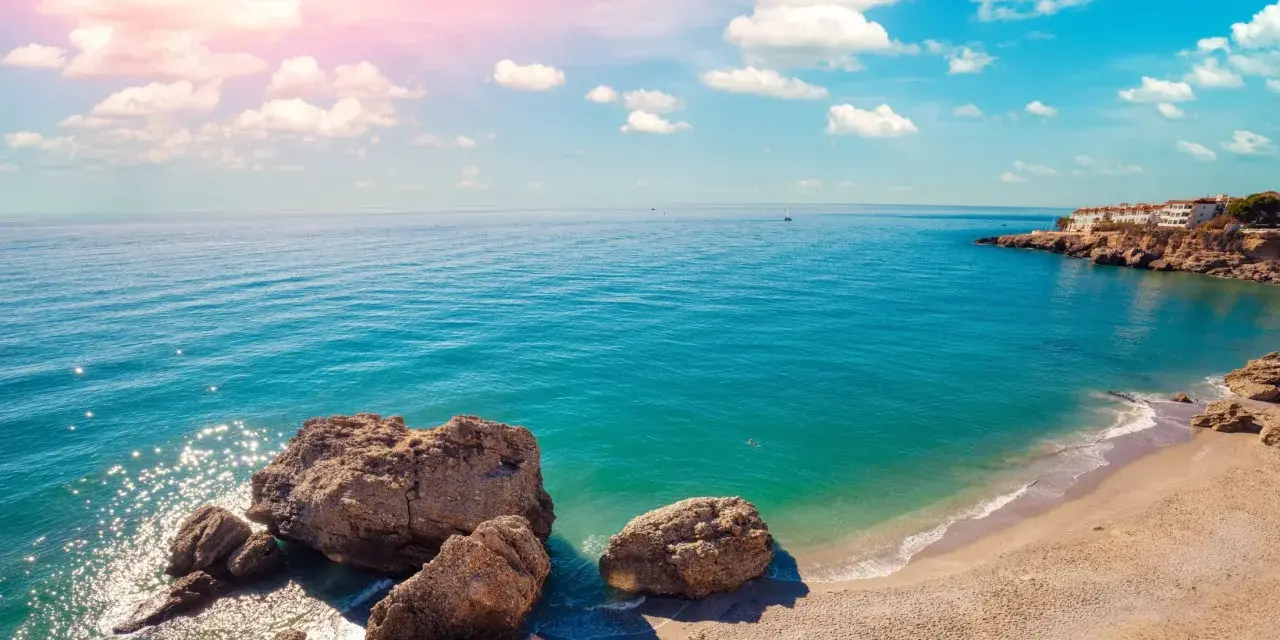 Piękne wybrzeże Costa del Sol z białymi domkami na klifie, turkusowym morzem i skalistą plażą. Idealne miejsce na wakacje!