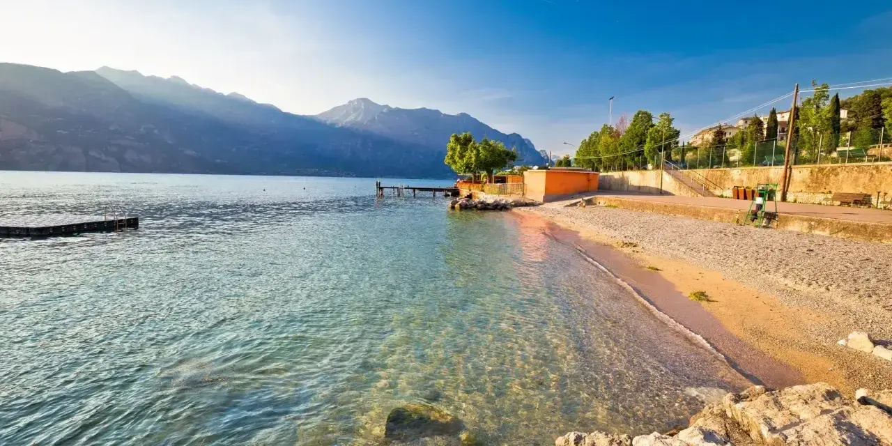 Słoneczna plaża nad jeziorem Garda z kamienistym brzegiem i łagodnymi falami.