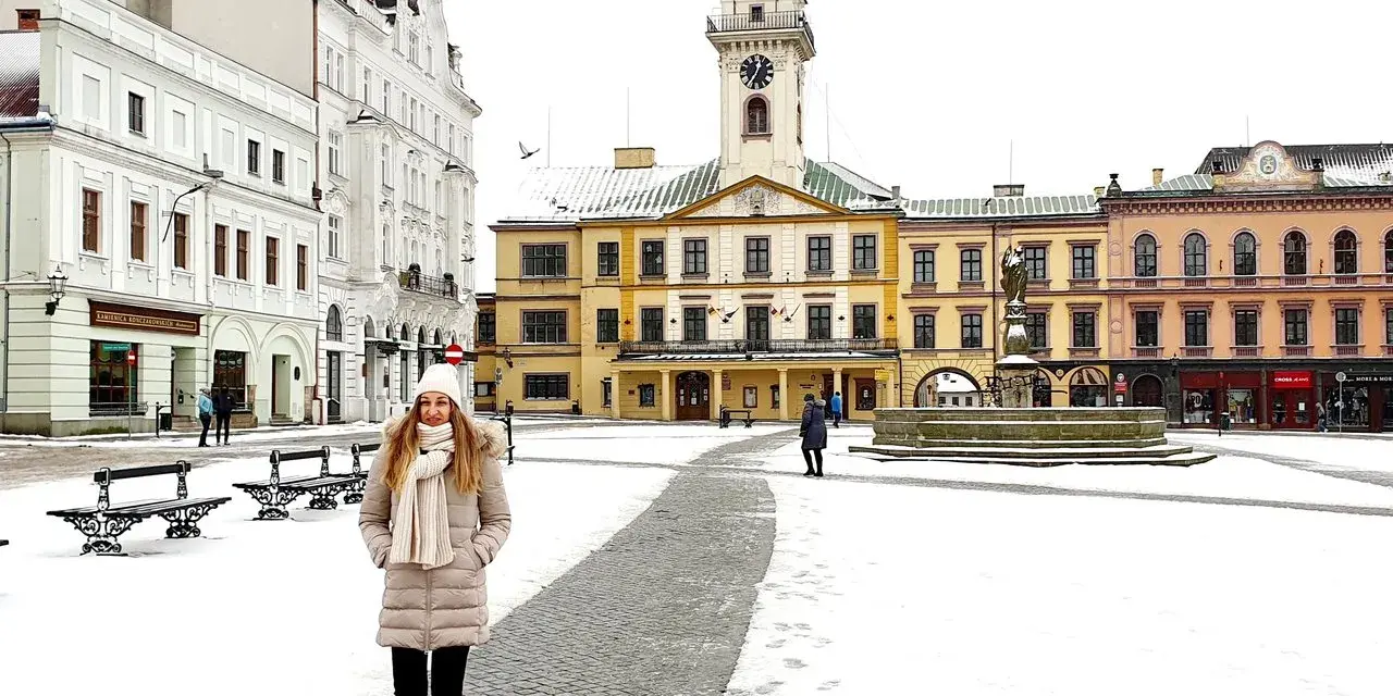 Zimowy spacer po Rynku w Cieszynie. Kobieta w ciepłym ubraniu przemierza ośnieżony plac, podziwiając zabytkowe kamienice i ratusz. Idealny pomysł na cieszyn w jeden dzień.