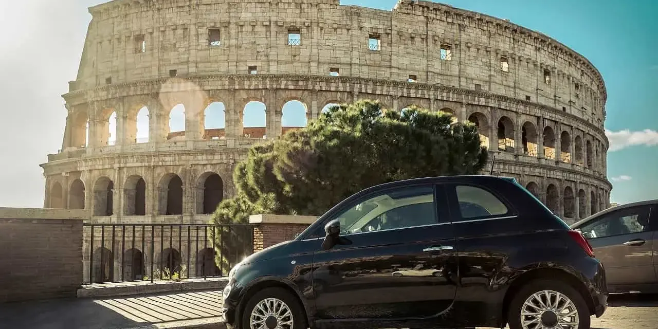 Czarny Fiat 500 pod Koloseum w Rzymie. Zastanawiasz się, ile się jedzie z Polski do Włoch samochodem?