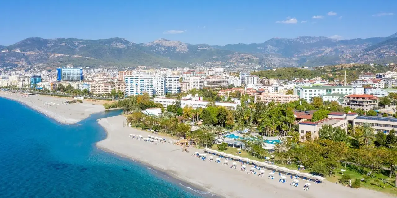 Widok z lotu ptaka na kurort nad morzem w Turcji z plażą, hotelami i górami w tle.