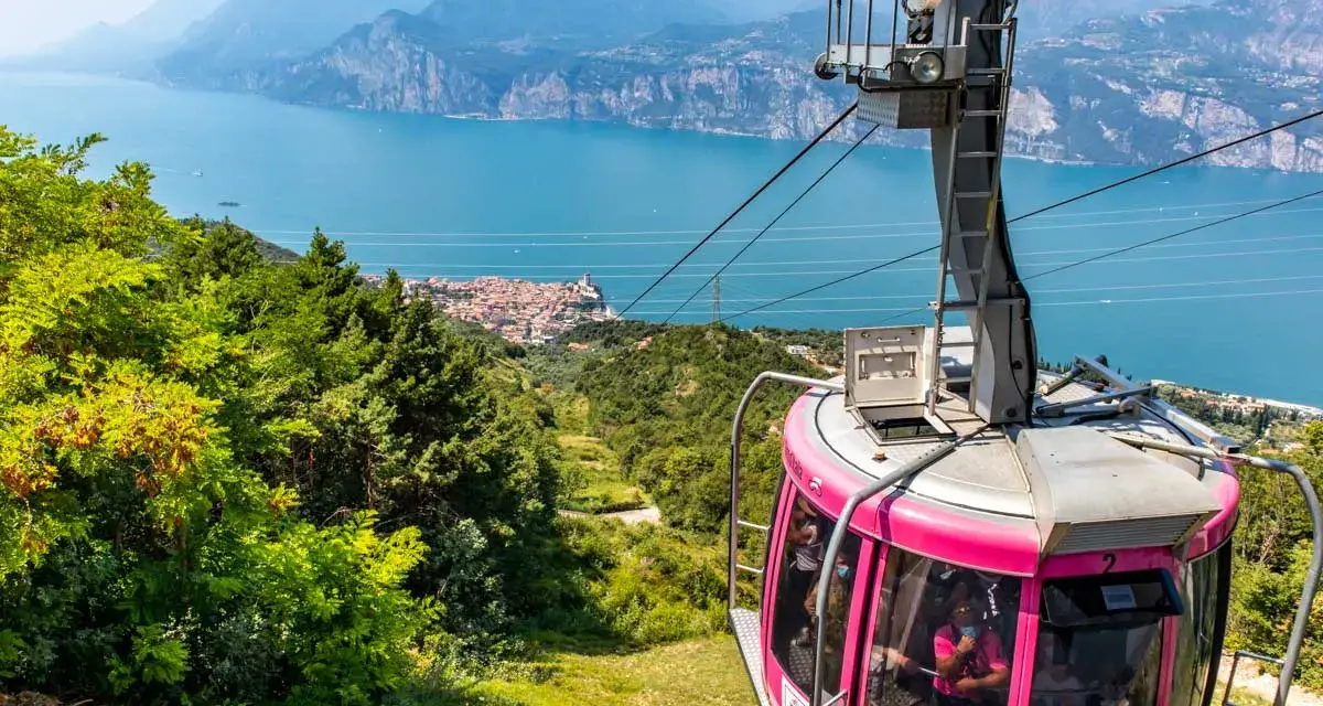 Różowa kolejka linowa Monte Baldo zjeżdża w dół, oferując widok na jezioro Garda i malownicze miasteczko.