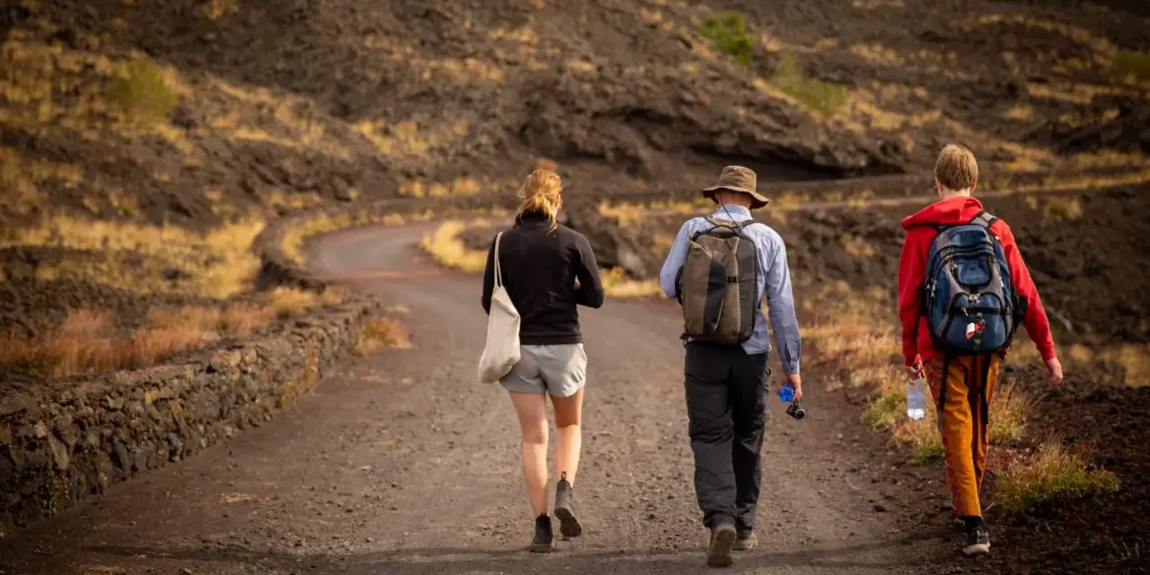 Trzy osoby wędrują po wulkanicznym krajobrazie Sycylii. Styczeń na wyspie oferuje przyjemną temperaturę do trekkingu.